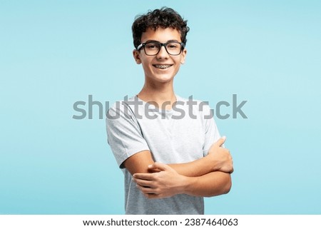 Portrait of smiling attractive teenage boy wearing eyeglasses with crossed arms looking at camera isolated on blue background. Vision, health care Royalty-Free Stock Photo #2387464063