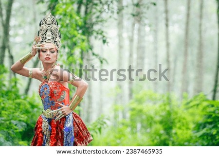 Portrait of an Indonesian woman wearing Payas Agung Bali or red traditional Balinese cultural clothing with lots of gold ornaments or props. Take photos with an outdoor forest background.