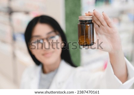 Focused shot of asian young female druggist pharmacist in white medical coat looking at medicine drug jar, pills, remedies, painkillers, vitamins in pharmacy drugstore Royalty-Free Stock Photo #2387470161