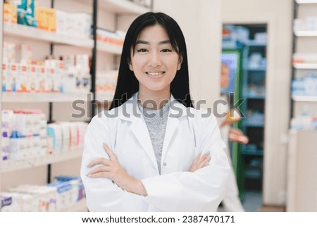 Closeup photo of asian female confident successful young pharmacist druggist in white medical coat standing with arms crossed at the cash point desk in pharmacy drugstore Royalty-Free Stock Photo #2387470171