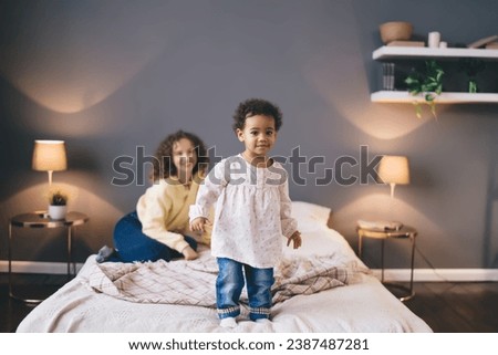 Positive little girl standing on bed in bedroom