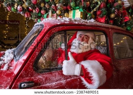 Portrait of Santa Claus driving a red car at Christmas and showing thumbs up. 