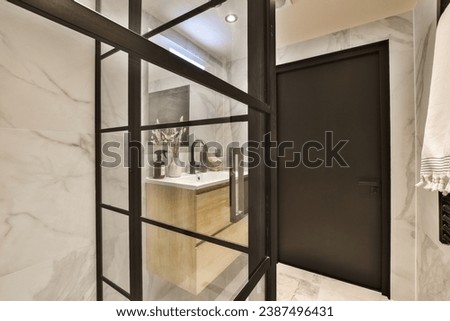 a bathroom with white marble walls and black trim around the shower door, which is open to reveal a large mirror Royalty-Free Stock Photo #2387496431