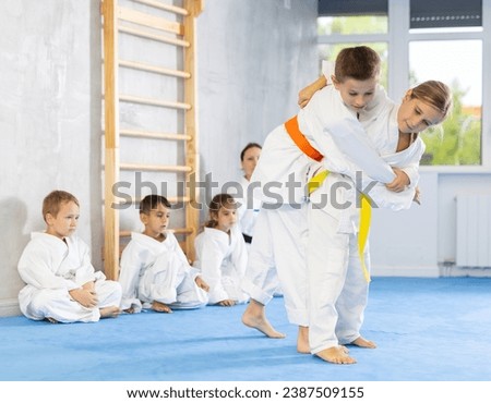 Young boys and girls athletes in white kimonos practice Brazilian jiu Jitsu Aikido Wing chun wrestling. Training at Academy of Martial Arts martial arts hand-to-hand combat. Royalty-Free Stock Photo #2387509155