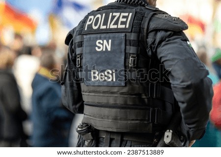 An unrecognizable german police officer stands nearby a demonstration, Polizei is the german word for police Royalty-Free Stock Photo #2387513889