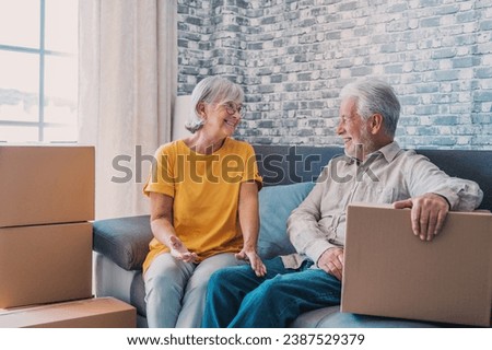 Relaxed mature married couple in love resting on couch among paper cardboard boxes, taking break, pause, hugging, talking, enjoying being in new home. Real estate concept Royalty-Free Stock Photo #2387529379