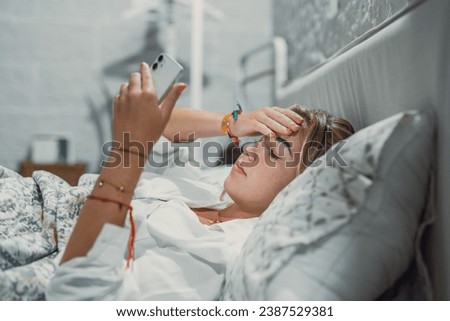 Top view unhappy woman feeling headache after sudden awakening by phone call, message signal or alarm in early morning, exhausted young female suffering from insomnia or migraine, lying in bed Royalty-Free Stock Photo #2387529381