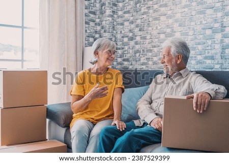 Relaxed mature married couple in love resting on couch among paper cardboard boxes, taking break, pause, hugging, talking, enjoying being in new home. Real estate concept Royalty-Free Stock Photo #2387529399