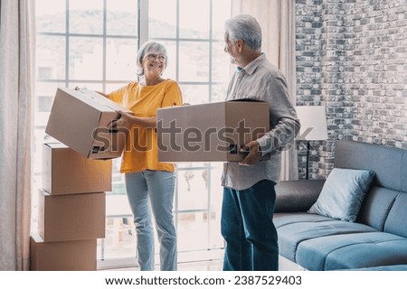 Mature couple moving into new apartment, carrying cardboard boxes into empty room with potted plants. Real estate property buying, relocation, new home concept. Rear view Royalty-Free Stock Photo #2387529403