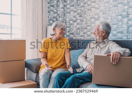 Relaxed mature married couple in love resting on couch among paper cardboard boxes, taking break, pause, hugging, talking, enjoying being in new home. Real estate concept Royalty-Free Stock Photo #2387529469