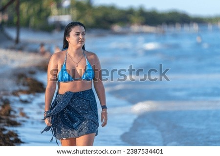 Woman enjoying an idyllic walk along a caribbean beach gazing the sea wearing sarong and bikini