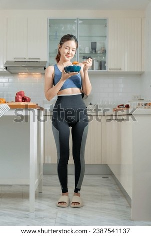 A healthy Asian woman in exercise clothes Is happily cooking a healthy meal in her home kitchen in the morning. Healthy care concept, Healthy fruits every day. Royalty-Free Stock Photo #2387541137