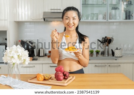 A healthy Asian woman in exercise clothes Is happily cooking a healthy meal in her home kitchen in the morning. Healthy care concept, Healthy fruits every day. Royalty-Free Stock Photo #2387541139