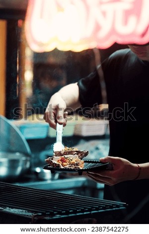 Oysters are fried on a grill. Chef prepares a dish at grill grate, Oriental cuisine