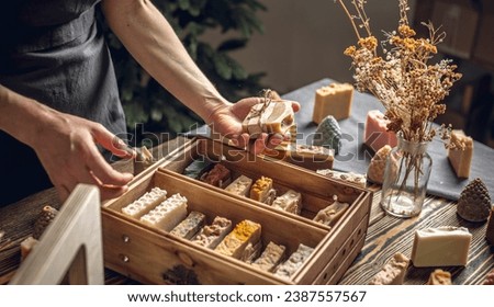 A woman soap maker holds handmade soap in her hands. A lot of different sliced pieces in a wooden box. Eco-friendly natural handmade cosmetics.