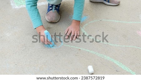 Cute schoolgirl drawing on asphalt with colored chalks