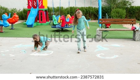Two cute schoolgirl girls drawing on asphalt with colored chalks