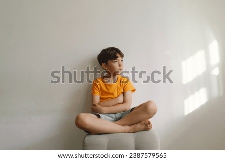 Cute boy sitting barefoot in a home. Beautiful light. Brunette boy 7 years old, casual clothes. Cozy home and lifestyle. Indoors. Royalty-Free Stock Photo #2387579565