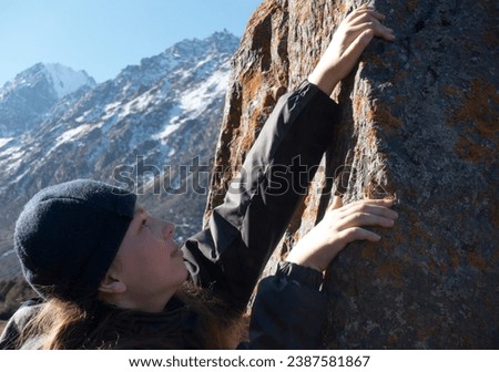 Boy climbs a rock against the snow winter mountains. Children rock climbing. Extreme hobby trains.