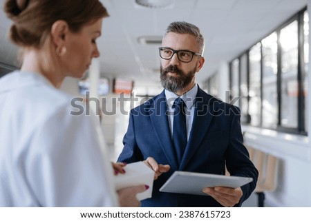 Pharmaceutical sales representative talking with female doctor in medical building. Hospital director consulting with healthcare staff. Royalty-Free Stock Photo #2387615723
