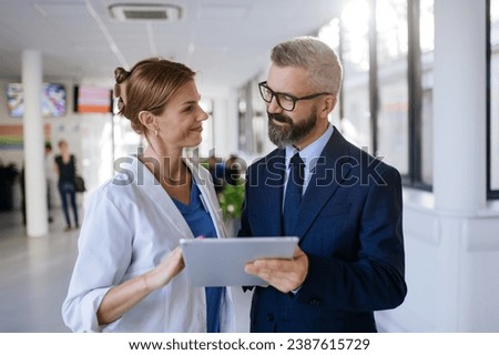 Pharmaceutical sales representative talking with female doctor in medical building. Hospital director consulting with healthcare staff. Royalty-Free Stock Photo #2387615729