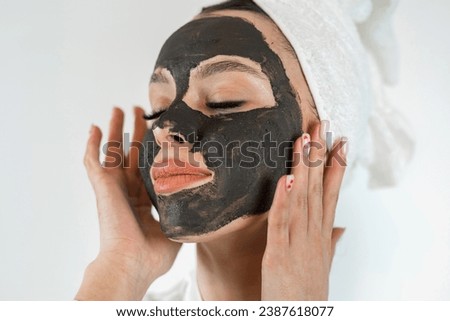 Young pretty woman doing cosmetic anti aging treatment with black clay mask on her face, spa procedure. Skin care