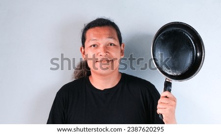 Portrait of an asian man holding frying pan in front of white background