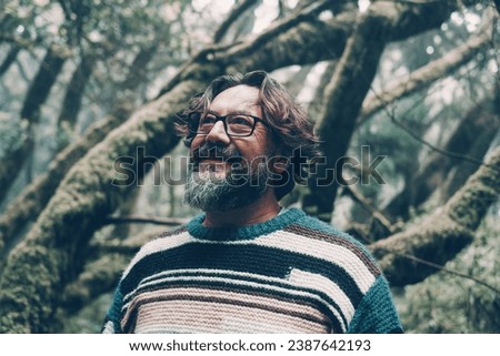 Handsome mature man smile in outdoor leisure activity with green nature forest in background. People and connection with woods. Moody color image of person wearing eyewear and smiling outside at park