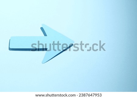 One paper arrow on light blue background, above view. Space for text