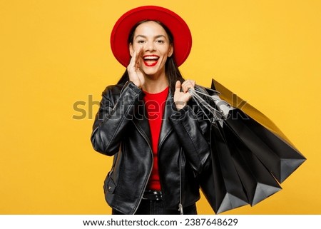 Young woman wear casual clothes red hat hold shopping paper package bags scream sharing hot news about sales with hand near mouth isolated on plain yellow background. Black Friday sale buy day concept Royalty-Free Stock Photo #2387648629