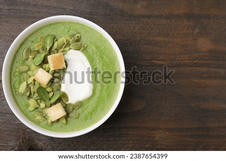 Delicious broccoli cream soup with croutons, sour cream and pumpkin seeds on wooden table, top view. Space for text