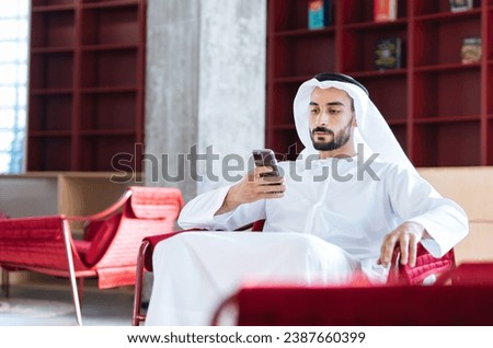 handsome man with dish dasha working in his business office of Dubai. Portraits of a successful businessman in traditional emirates white dress. Concept about middle eastern cultures. Royalty-Free Stock Photo #2387660399