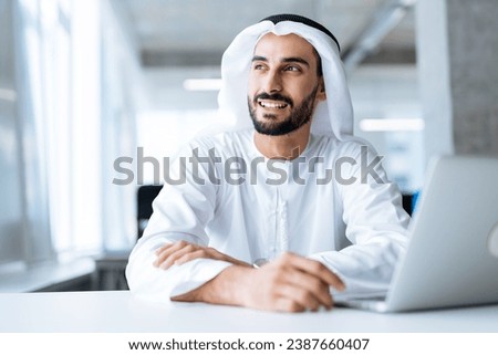 handsome man with dish dasha working in his business office of Dubai. Portraits of a successful businessman in traditional emirates white dress. Concept about middle eastern cultures. Royalty-Free Stock Photo #2387660407