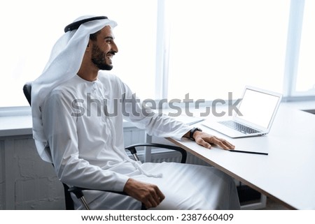 Handsome man with dish dasha working in his business office of Dubai. Portraits of a successful businessman in traditional emirates white dress. Concept about middle eastern cultures. Royalty-Free Stock Photo #2387660409