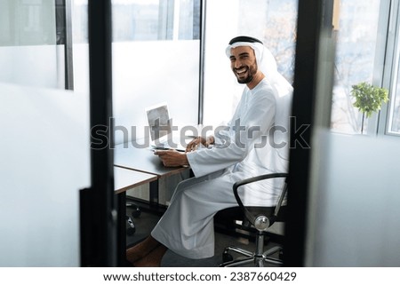handsome man with dish dasha working in his business office of Dubai. Portraits of a successful businessman in traditional emirates white dress. Concept about middle eastern cultures. Royalty-Free Stock Photo #2387660429