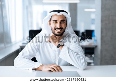 handsome man with dish dasha working in his business office of Dubai. Portraits of a successful businessman in traditional emirates white dress. Concept about middle eastern cultures. Royalty-Free Stock Photo #2387660431