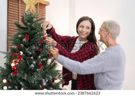 Mother and daughter are excited and happy to decorate the Christmas tree at home during the holiday season. Spending time together at Christmas