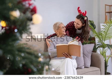 Cute young woman holds a gift box to surprise his mother on Christmas Day. 60 year old retired woman happy Happy daughter on Christmas day in living room holding red gift box