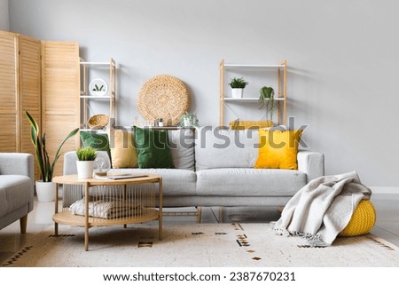 Cozy grey sofa, coffee table and pouf with soft blanket in interior of living room Royalty-Free Stock Photo #2387670231