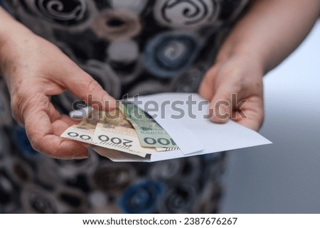 An elderly woman puts money, Polish banknotes pln, into an envelope