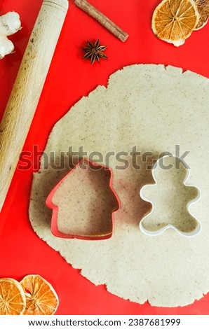 Gingerbread cookie dough rolled out on a red silicone mat, with house and man cookie cutters. Preparation of festive pastries. Vertical orientation.
