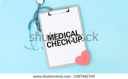 Grey stethoscope and paper plate with a sheet of white paper with text MEDICAL CHECK-UP light blue background. Medical concept.