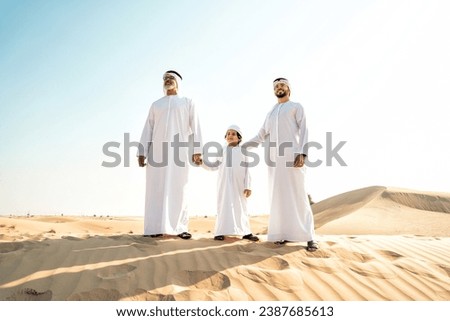 Three generation family making a safari in the desert of Dubai wearing white kandura outfit. Grandfather, son and grandson spending time together in the nature. Royalty-Free Stock Photo #2387685613