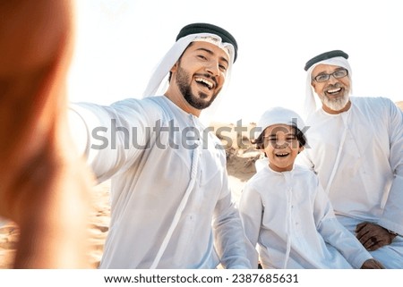 Three generation family making a safari in the desert of Dubai wearing white kandura outfit. Grandfather, son and grandson spending time together in the nature. Royalty-Free Stock Photo #2387685631