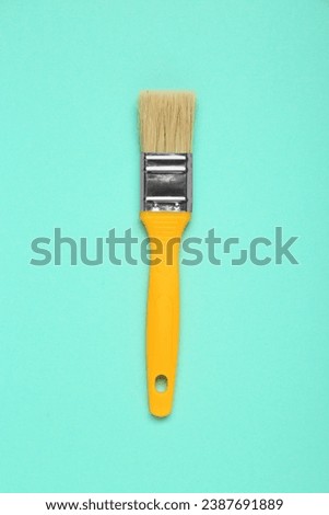 One paint brush with yellow handle on turquoise background, top view