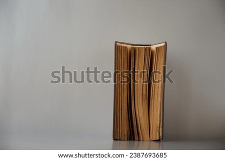 An old half-open book stands on a gray background. Theme of religion or antiquity, profound truths or commonplace truths Royalty-Free Stock Photo #2387693685