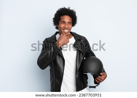young black afro man smiling with a happy, confident expression with hand on chin, wondering and looking to the side