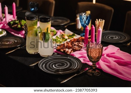 Served banquet table ready for guests, table with plate, glasses, forks, napkins. Luxury reception for a hen party or bachelor party. Decor with pink candles, tablecloth. Elegant table in party area.