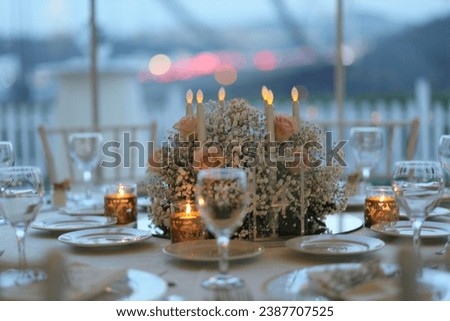 Decorated white wedding table for a festive dinner with pink flowers in brass pots on green lawn under the open sky. Royalty-Free Stock Photo #2387707525