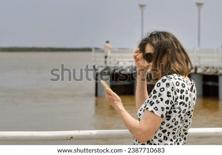 Senior tourist woman takes selfies on the river coast.